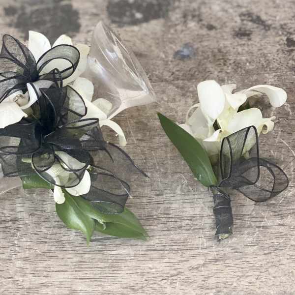 White orchid corsages with black ribbon bows on a wood surface