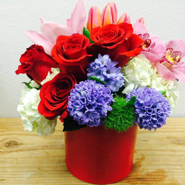 Red roses, purple blooms, and pink orchids in a red vase