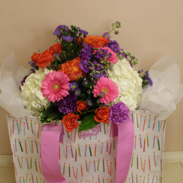 Colorful bouquet in a patterned gift bag with pink ribbon