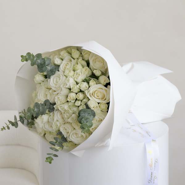 Bouquet of white roses wrapped in white paper with eucalyptus