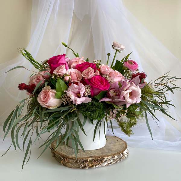 Pink rose bouquet in a white vase with trailing greenery