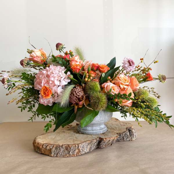 Low floral arrangement in a metal urn with peach and pink blooms