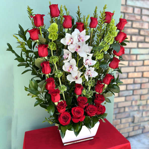 Tall arrangement of red roses and white orchids in a white vase