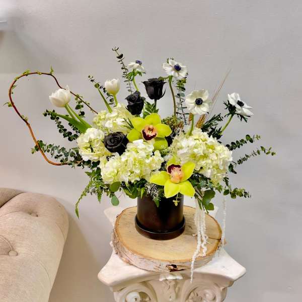 White and black floral arrangement with yellow orchids in a dark vase