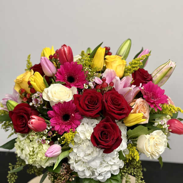 Mixed bouquet of roses, tulips, gerbera daisies, lilies, and hydrangea in a glass vase