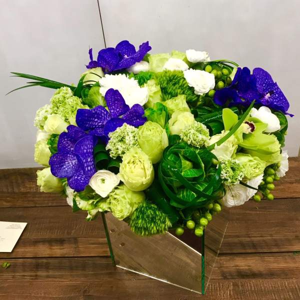 Green and white floral arrangement with purple orchids in a clear vase