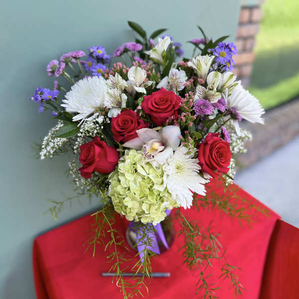 Bouquet of red roses, white blooms, and purple flowers in a vase