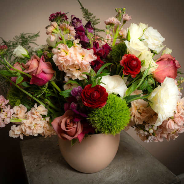 Mixed bouquet of roses, ranunculus, and stock in a beige vase