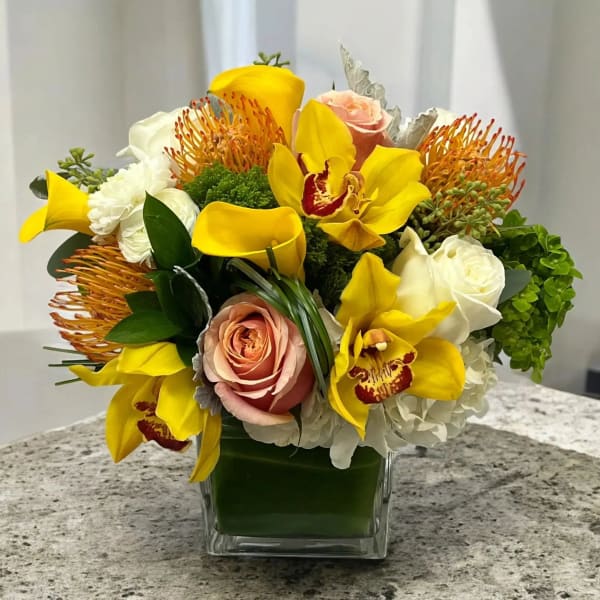 Yellow orchids and roses arranged in a square glass vase