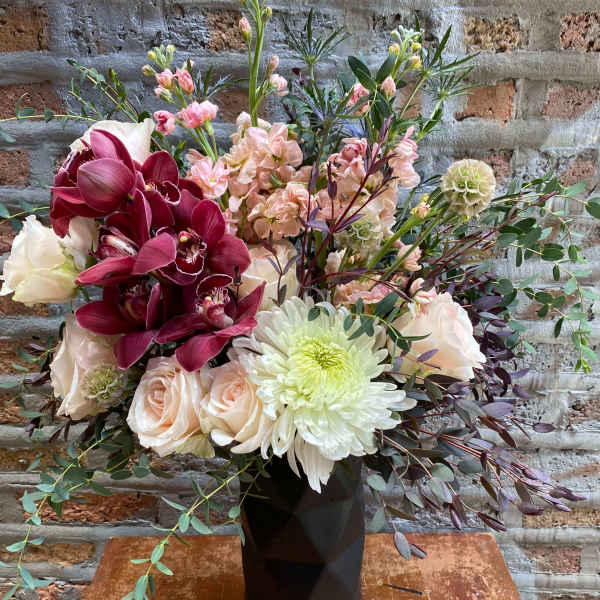 Mixed bouquet in a black vase with burgundy orchids and pale roses