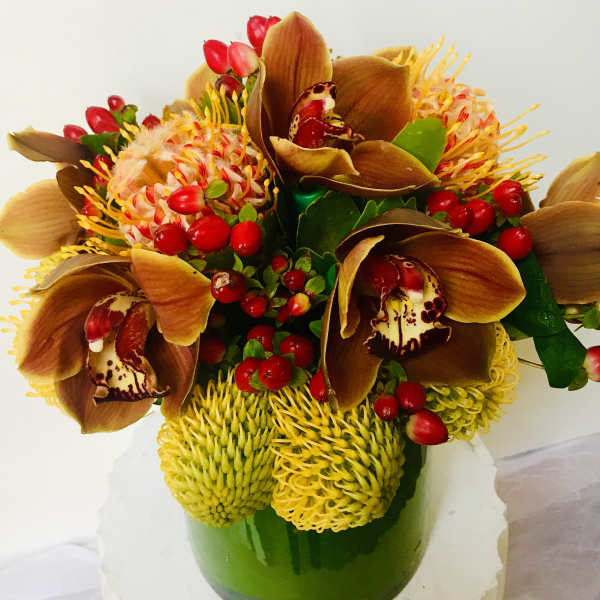 Bouquet with brown orchids, yellow pincushion blooms, and red berries in a green vase