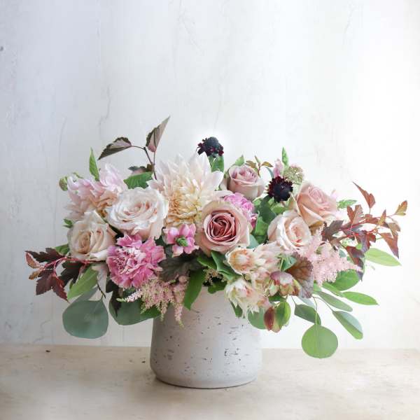 Low floral arrangement of blush roses and pale blooms in a white vase