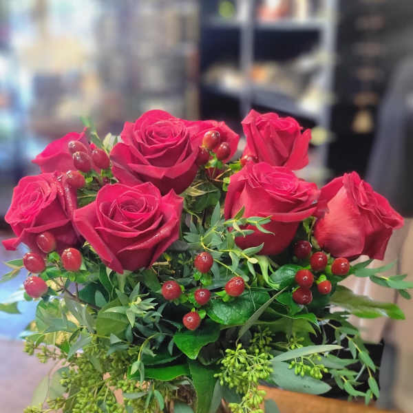 Red roses arranged in a clear glass vase with berry accents