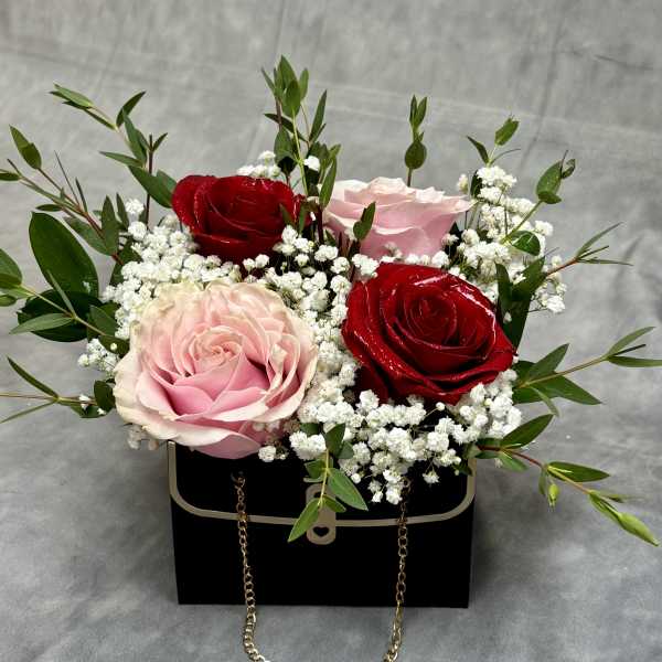 Pink and red roses arranged in a black box with white filler flowers