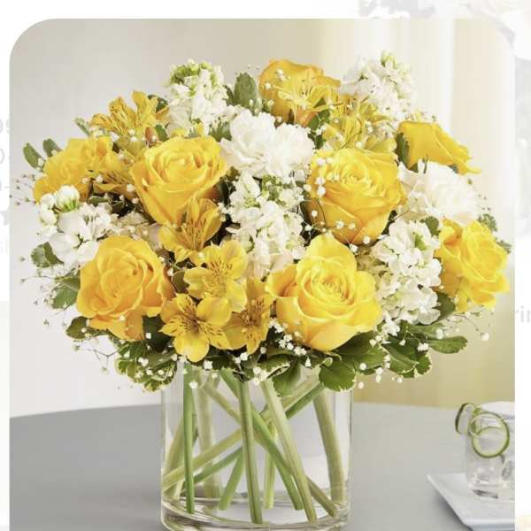 Yellow roses and white flowers arranged in a clear glass vase