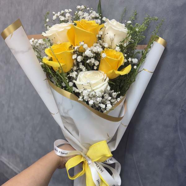 Bouquet of yellow and white roses wrapped in white paper with a yellow ribbon