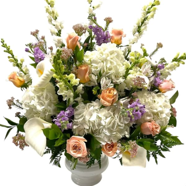 White hydrangeas, peach roses, and calla lilies in a white vase