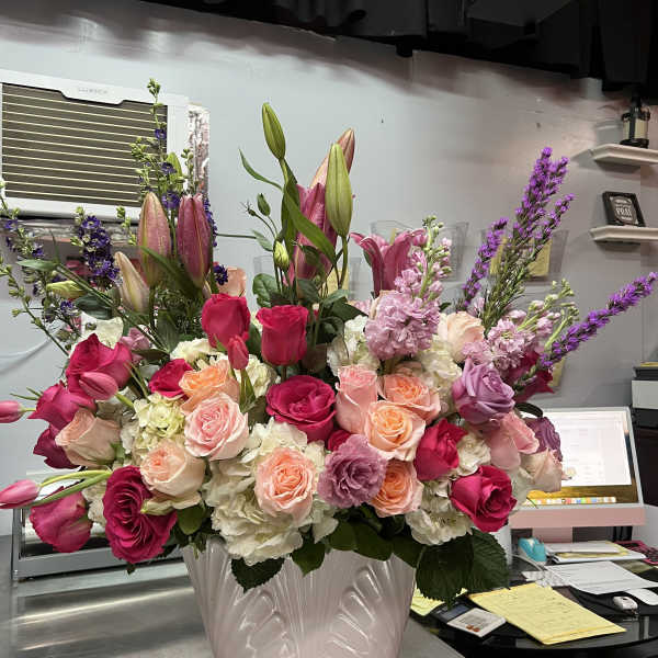 Large arrangement of pink lilies and roses with white hydrangeas in a pale pink ceramic vase