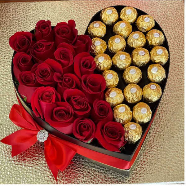 Heart-shaped box filled with red roses and gold-wrapped chocolates with a red bow