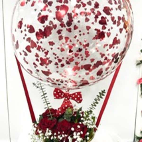 Heart-patterned balloon above a red rose arrangement in a gold vase