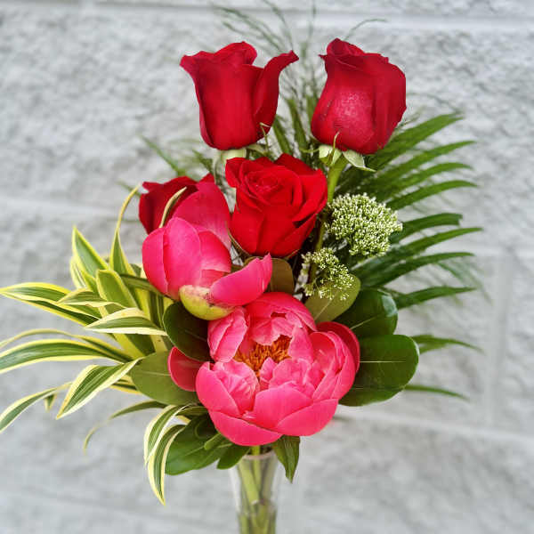 Red roses and a pink peony in a clear vase