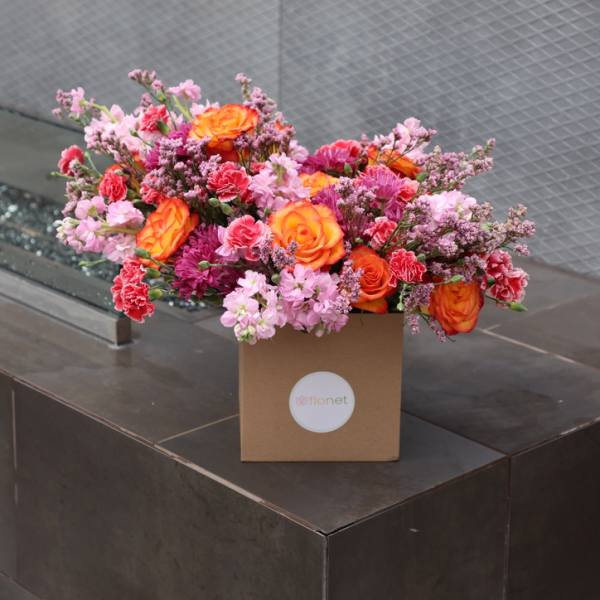 Pink and orange mixed flower arrangement in a brown box
