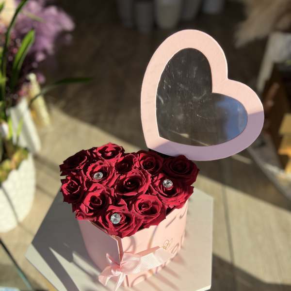 Heart-shaped box of red roses with a pink heart topper