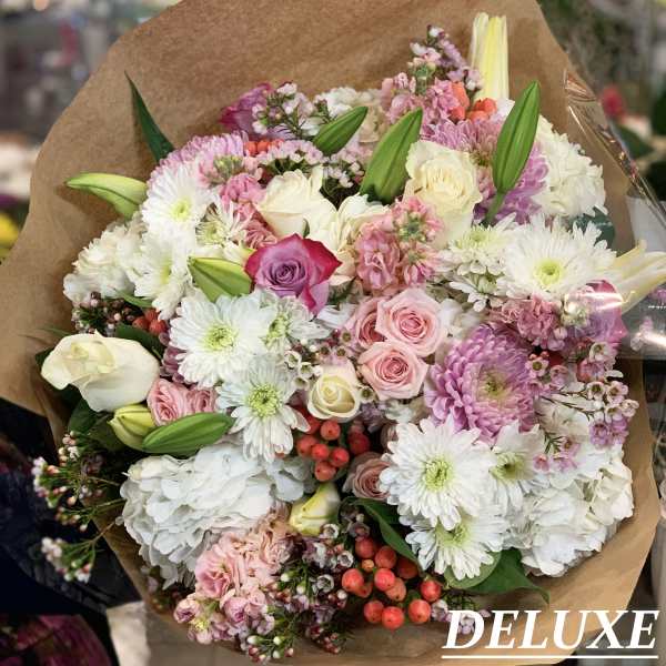Mixed bouquet of pink, white, and purple flowers wrapped in brown paper