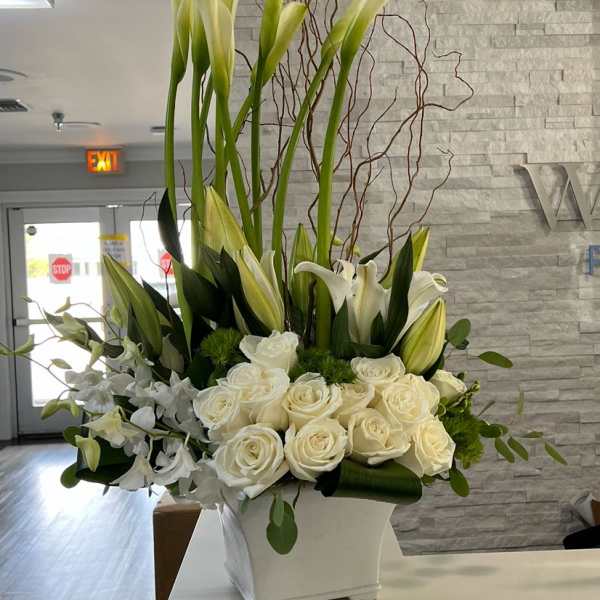Tall white arrangement with calla lilies, roses, orchids and curly branches in a square white vase