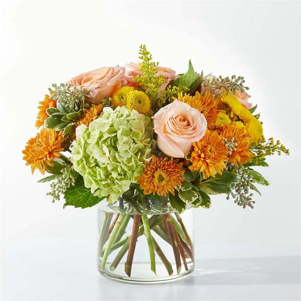Peach roses and orange mums in a clear glass vase with a green hydrangea bloom