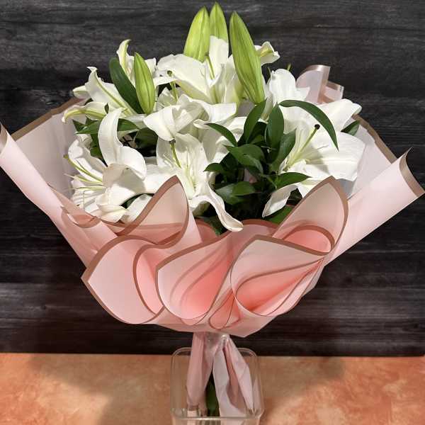 White lilies in pink wrapping with a clear vase