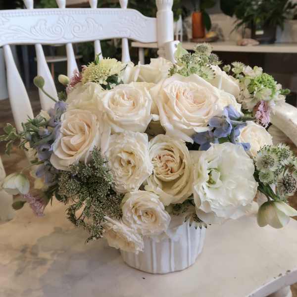 Cream rose bouquet in a white vase with small blue and green accent flowers