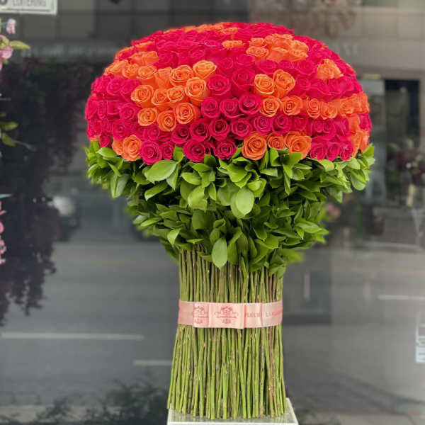 Large dome bouquet of pink and orange roses with a green leafy base