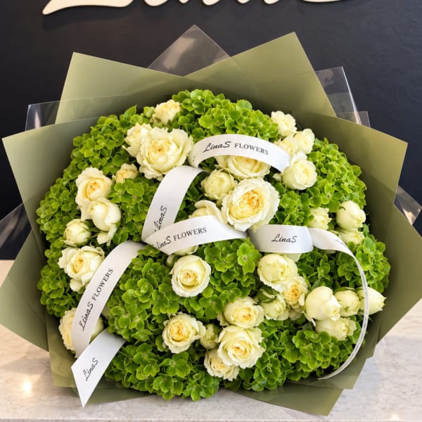 Bouquet of cream roses and green hydrangeas wrapped with branded ribbon