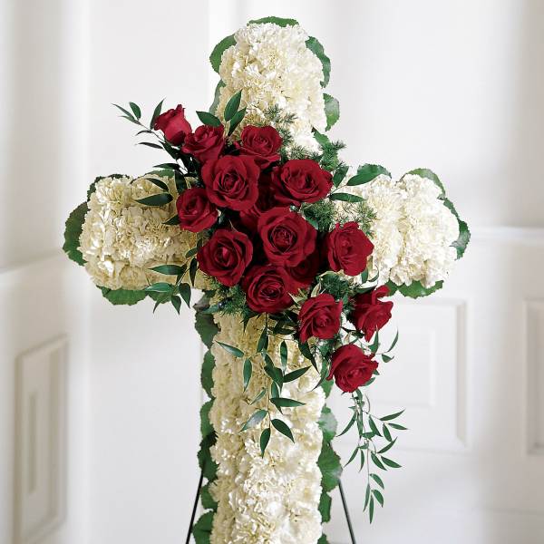 Red roses arranged on a white floral cross with a stand