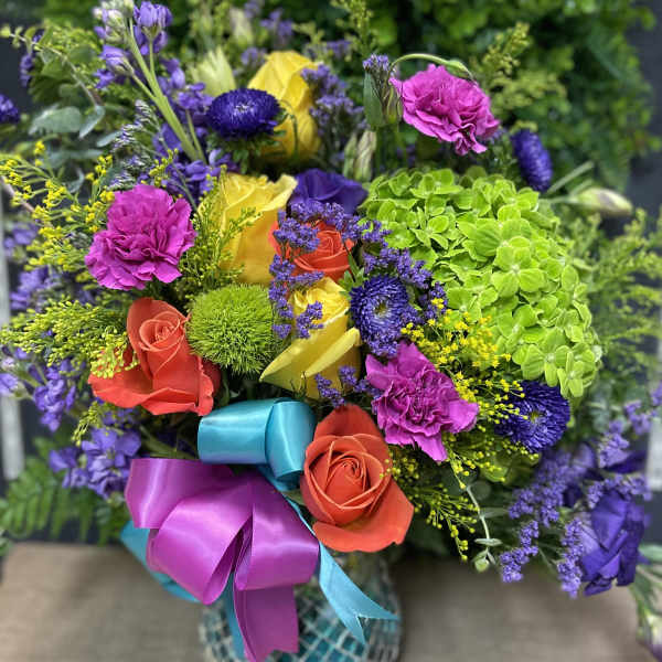 Colorful bouquet of roses, carnations, and purple blooms in a patterned vase