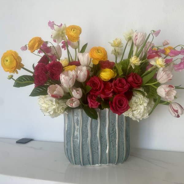 Mixed bouquet of roses, ranunculus, and tulips in a blue ceramic vase