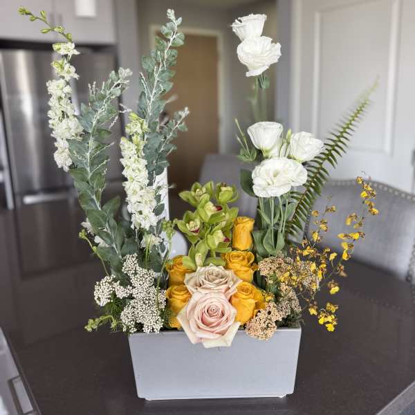 Mixed floral arrangement in a rectangular gray vase with white, yellow, and blush blooms