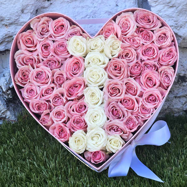 Heart-shaped box filled with pink and white roses and a ribbon bow