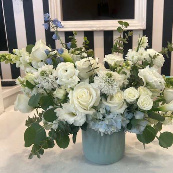 White roses and calla lilies in a pale blue vase with blue accents