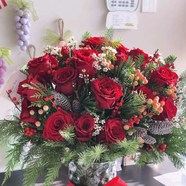 Red rose arrangement in a glass vase with pinecones and a red ribbon