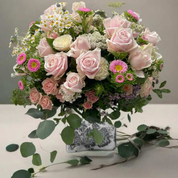 Pink roses and small daisies arranged in a square glass vase