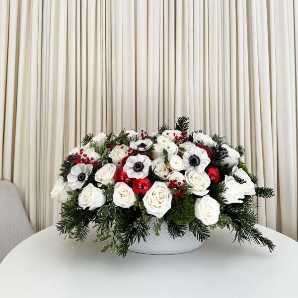 White rose arrangement with red accents in a white bowl vase