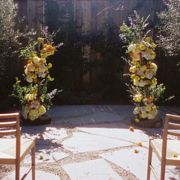 Two tall floral arrangements flank an outdoor ceremony space with chairs in front.