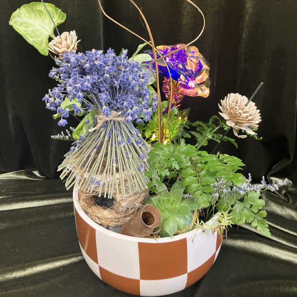 Mixed floral arrangement in a striped bowl with blue blooms and decorative accents