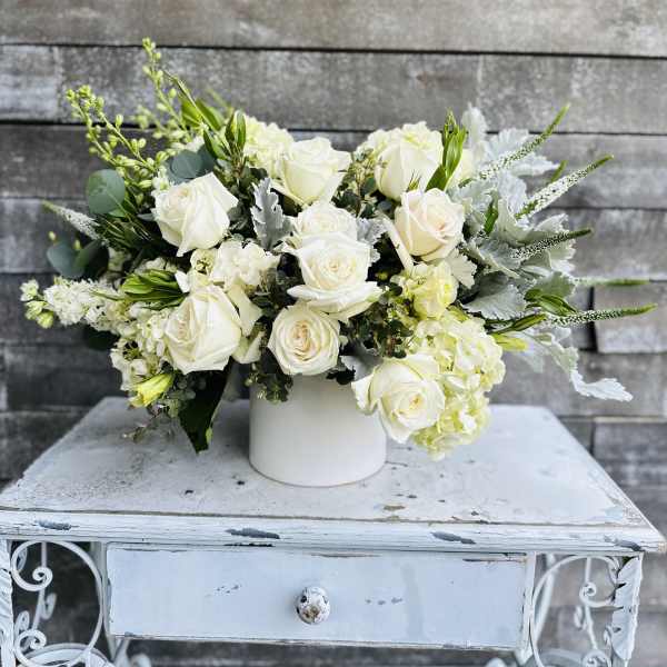 White rose arrangement in a white vase with silver foliage
