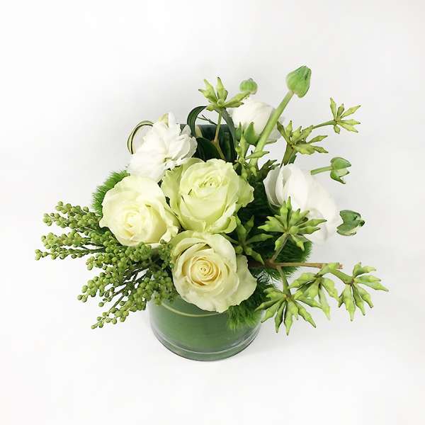 White roses arranged in a green glass vase with green accents