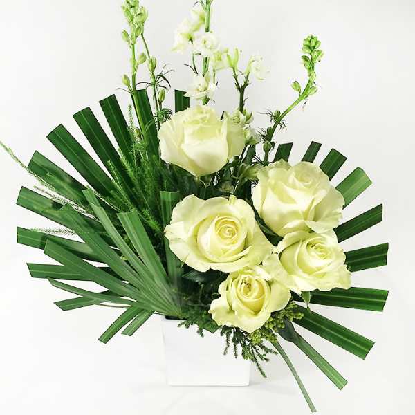 White roses arranged with tall white blooms in a white vase