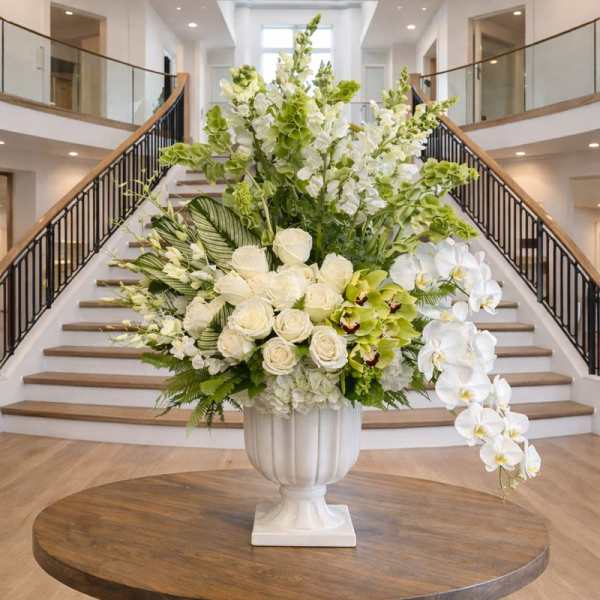Large white floral arrangement in a pedestal vase with cascading orchids