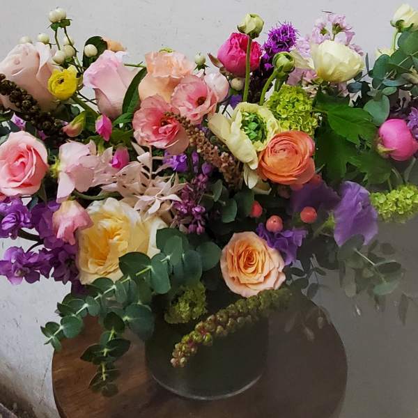 Large mixed bouquet of pink, peach, purple, and yellow flowers in a dark vase